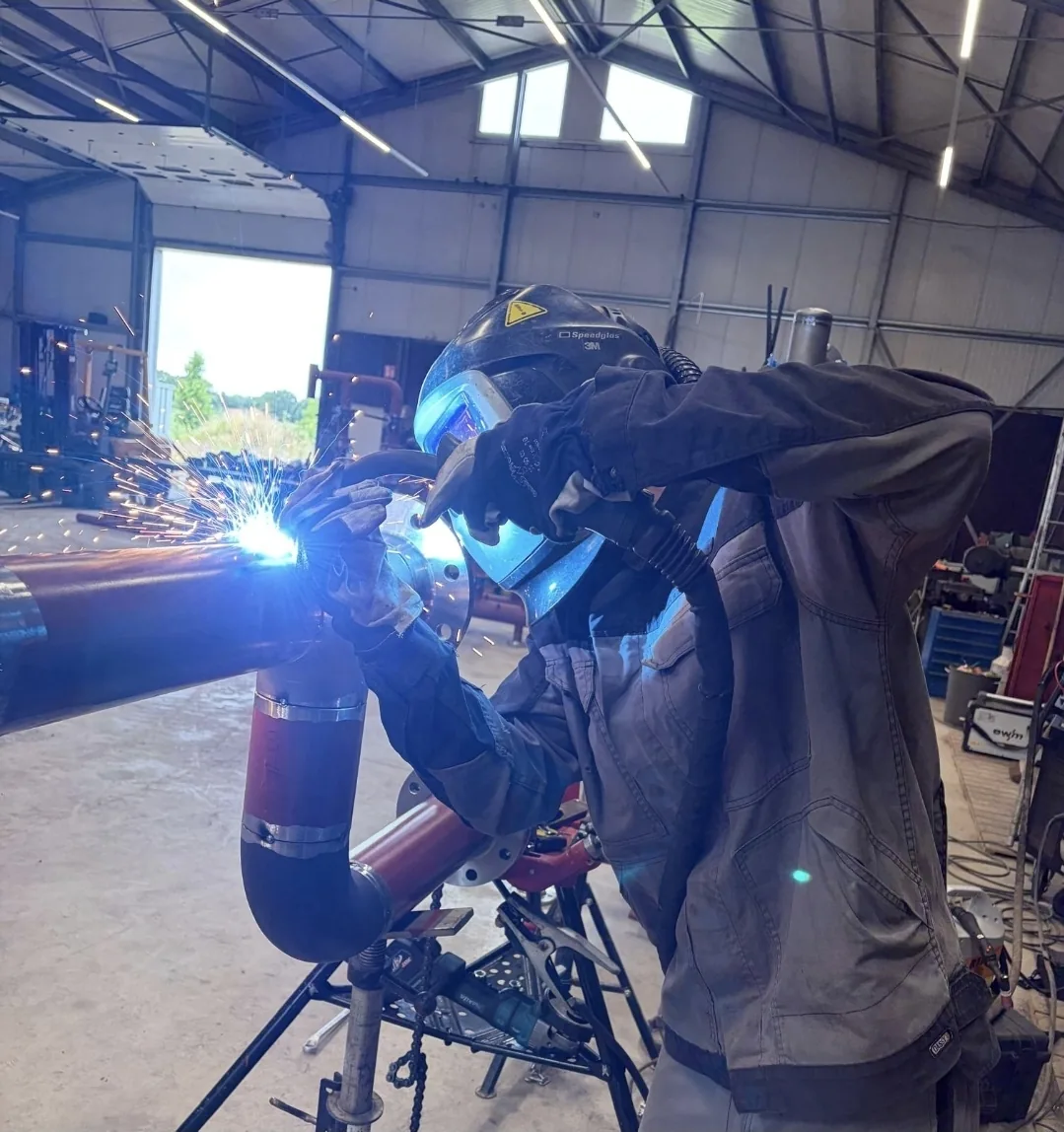 Lasser aan het werk aan een stalen buisconstructie, met vonken, in de werkplaats